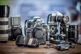 “A collection of professional camera equipment arranged on a table, including DSLR and mirrorless cameras, several lenses, memory cards, flashes, and other photography accessories.”