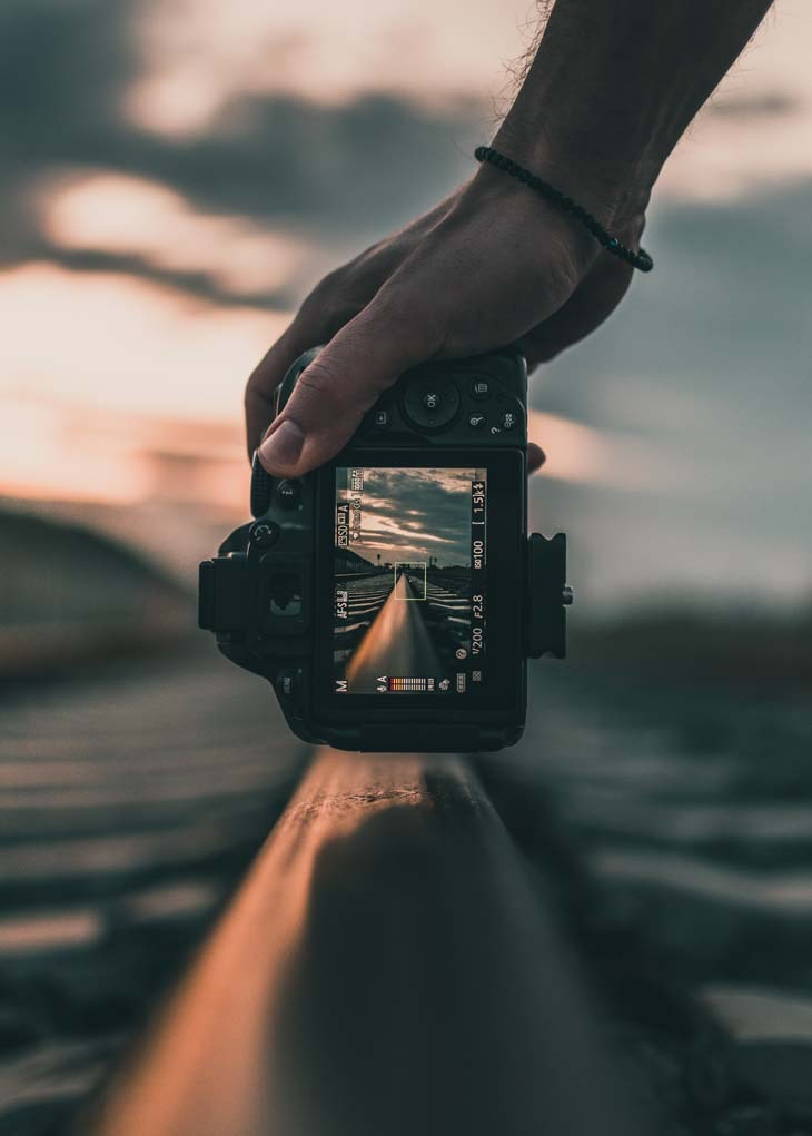 A man grabbing a camera sideways and taking a picture of a train track with only the screen being in focus.