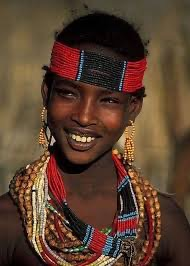 “A portrait of a young woman wearing traditional beaded jewelry and a red headband, smiling warmly.”